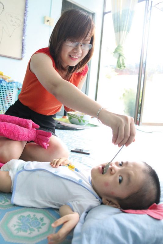 Cô Phan Thị Minh Nguyệt đút ăn cho bé Trương Hải An (2 tuổi) được bố mẹ ở Đức gửi về trung tâm ba tháng nay